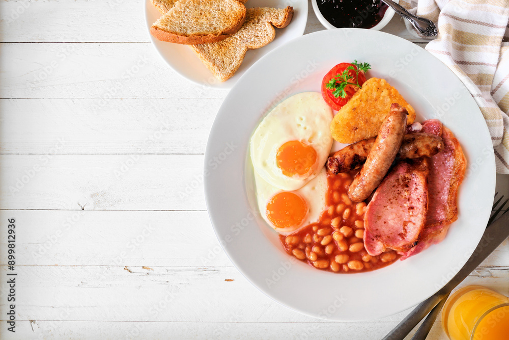 Full English breakfast with baked beans, bacon, eggs, sausage and hash browns. Above view table scene on a white wood background with copy space. Full English breakfast with baked beans, bacon, eggs, sausage and hash browns. Above view table scene on a white wood background with copy space.
