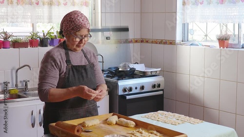 Senior latin woman kneading dough, cooking chilean fried sweet pastry calzones rotos in her domestic kitchen. 