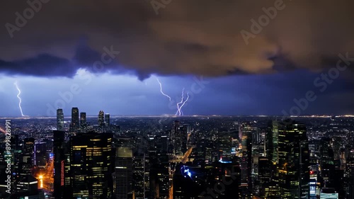 A dramatic cityscape at night, illuminated by a bright lightning bolt striking across the sky. The buildings stand tall against the dark stormy clouds. photo