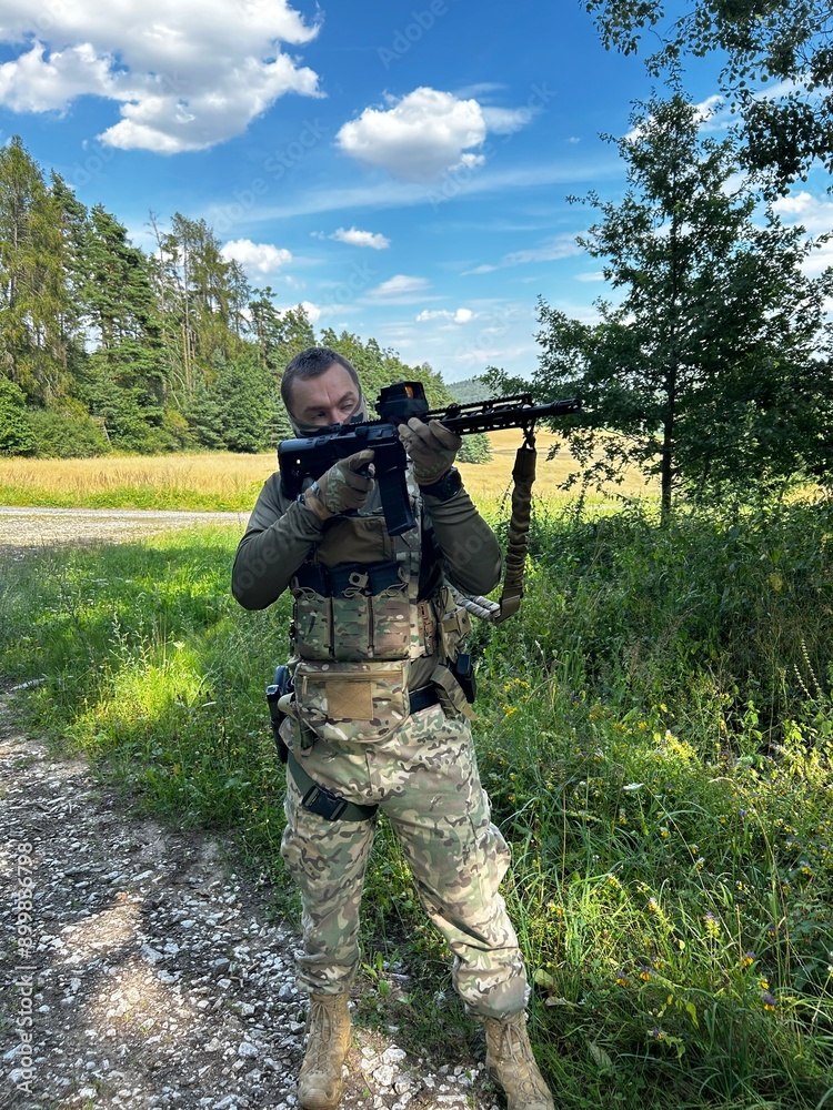 Fototapeta premium A soldier aiming a rifle. A soldier with a rifle in his hand standing in the forest. Dressed in camouflage.