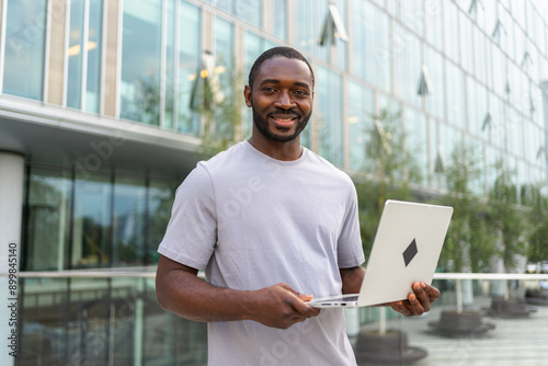 African American man freelancer using laptop typing chatting on urban street in city. Guy having virtual meeting online chat conference. Entrepreneur programmer working on laptop outdoors. Remote work © Юлия Завалишина