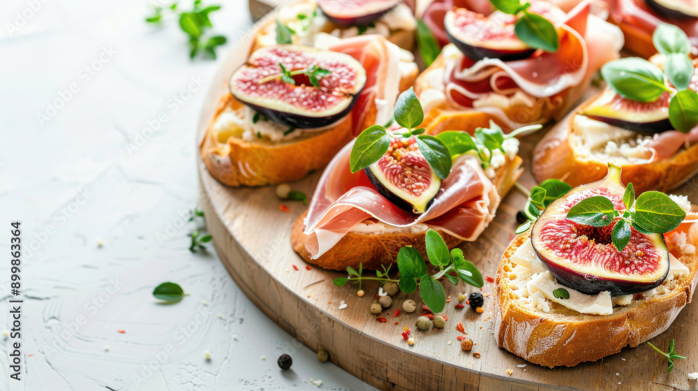 Delicious bruschettas with fig, cheese, prosciutto, and herbs on a wooden plate, copy space on white background, healthy breakfast idea. Top view. Delicious bruschettas with fig, cheese, prosciutto, and herbs on a wooden plate, copy space on white background, healthy breakfast idea. Top view.