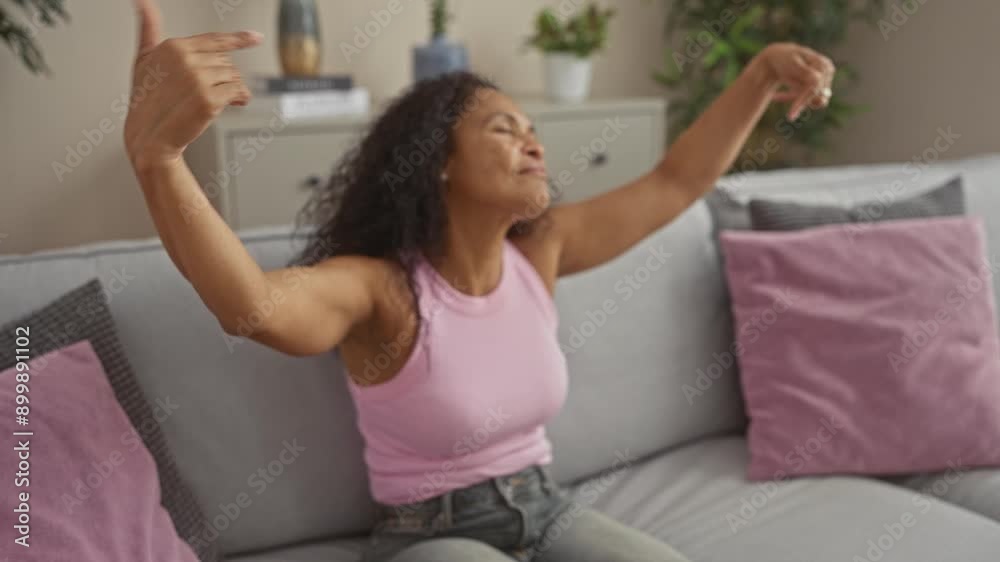 Woman dancing inside a living room with plants and cushions, wearing pink top and jeans, showing joy and relaxation. Woman dancing inside a living room with plants and cushions, wearing pink top and jeans, showing joy and relaxation.