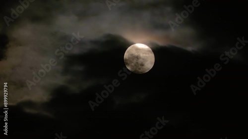 Supermoon in dark clouds. Full moon in the night cloudy sky close-up