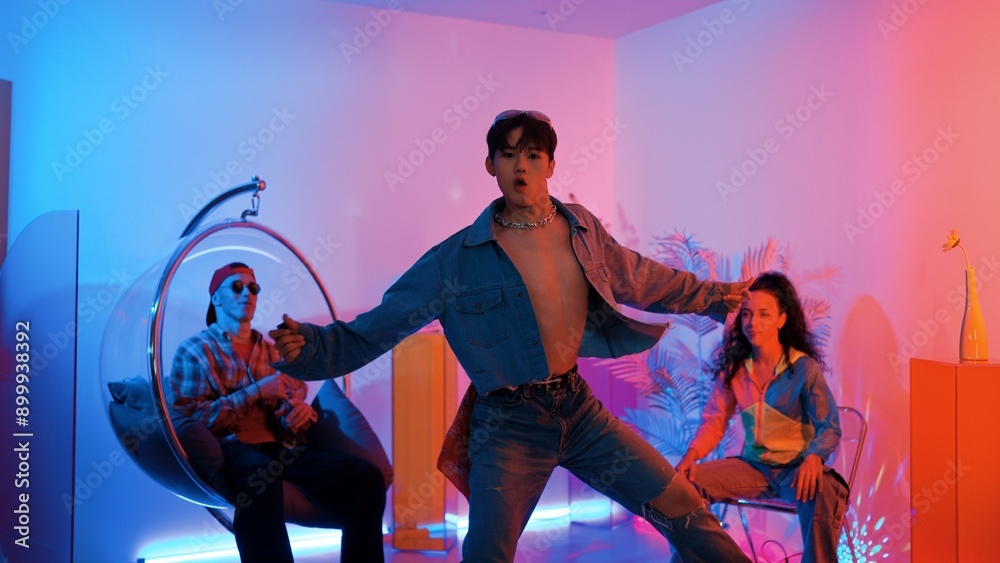 Fototapeta premium Skilled asian dancer moving to modern music while multicultural friend sitting at chair. Professional performer dancing show energetic foot step while hipster team cheering and supporting. Regalement.