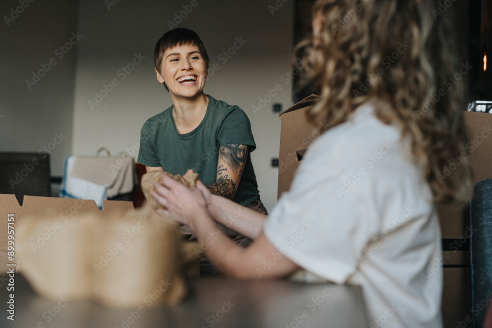 Happy lesbian woman sitting with girlfriend and wrapping stuff during relocation Happy lesbian woman sitting with girlfriend and wrapping stuff during relocation
