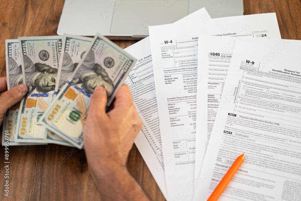 Obraz premium Person counting hundred-dollar bills while reviewing tax forms. Financial planning and tax preparation concept, ideal for tax season and accounting themes 