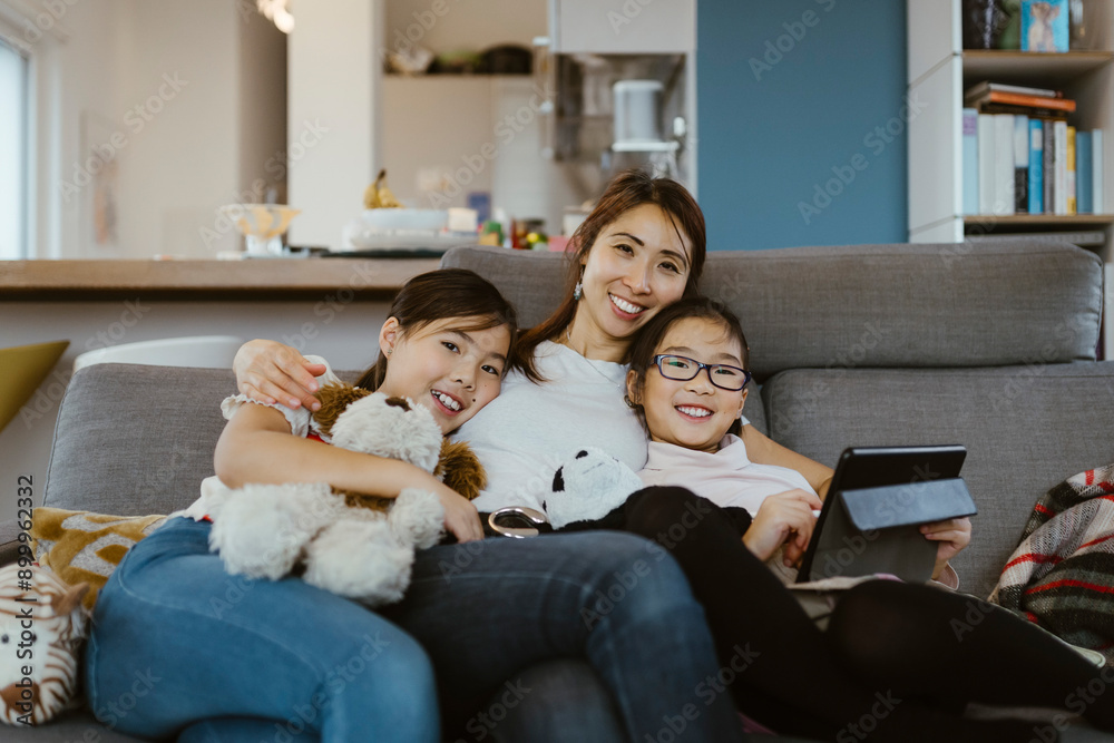 Portrait of smiling woman sitting with daughters on sofa at home Portrait of smiling woman sitting with daughters on sofa at home