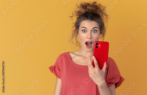 Excited Woman Looking at Phone in Front of Yellow Background