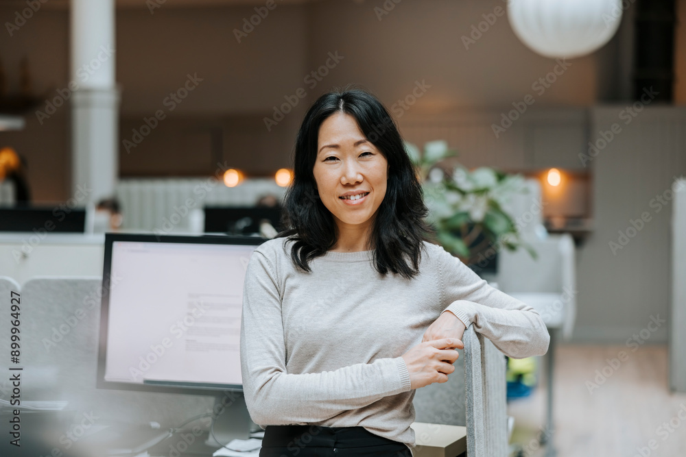 Smiling female entrepreneur leaning on desk while standing in office Smiling female entrepreneur leaning on desk while standing in office