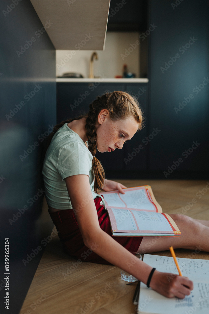 Girl with braided hair sitting on floor and doing homework at home Girl with braided hair sitting on floor and doing homework at home
