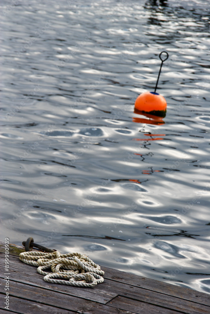Mooring hawser lying on a wooden jetty and a red buoy bobbing in the waters of the Skagerrak on the Swedish west coast in autumn. Mooring hawser lying on a wooden jetty and a red buoy bobbing in the waters of the Skagerrak on the Swedish west coast in autumn.