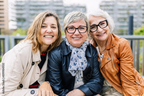 Portrait of three mature retired women smiling at camera sitting outside. Small group of mature females having fun at city street. Elderly friendship concept.