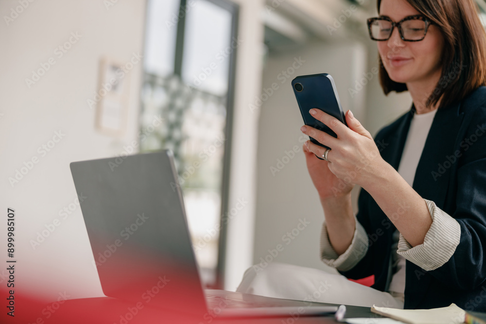 A confident businesswoman is using a smartphone and laptop in a modern office setting A confident businesswoman is using a smartphone and laptop in a modern office setting