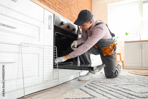 Male technician repairing electric oven in kitchen