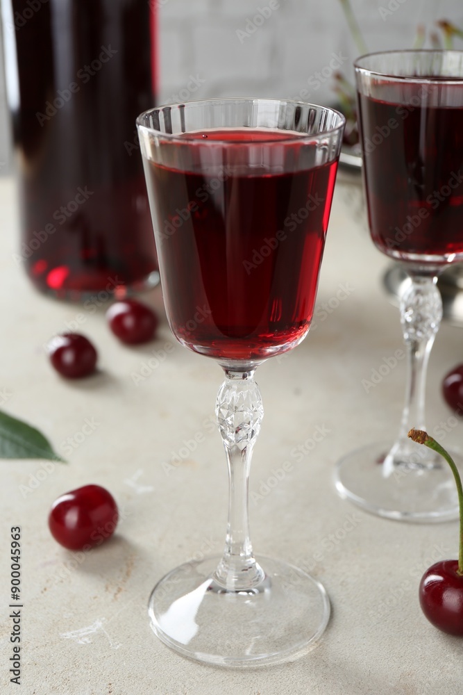 Delicious cherry liqueur in glasses and fresh berries on light grey table Delicious cherry liqueur in glasses and fresh berries on light grey table