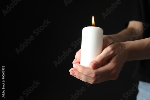 Woman holding burning candle on black background, closeup. Space for text