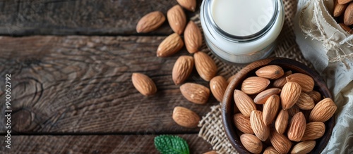 A bowl with almonds sits next to a glass bottle of almond milk on a table with a blank area for additional content in the image