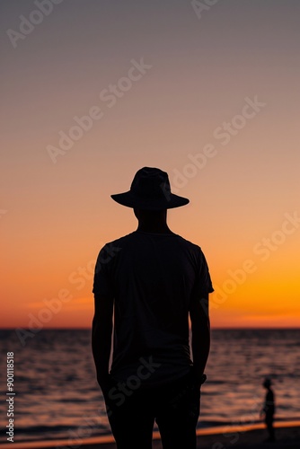 Silhouette of a man in a hat, standing by the ocean during sunset.