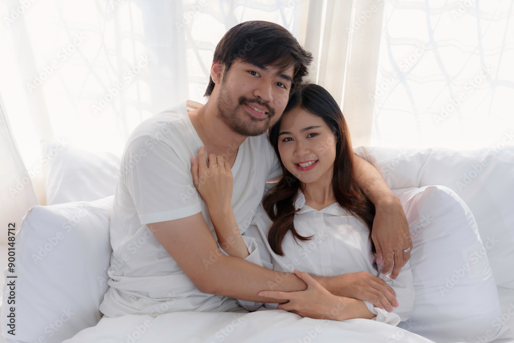 Young asian couple is embracing each other on the bed in a white bedroom with soft morning light Young asian couple is embracing each other on the bed in a white bedroom with soft morning light