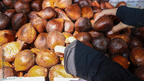 Close-up of a hand selecting salak fruit for sale at a market stall on sunny day. The fruit is known for its unique scaly skin and sweet, slightly tart flavor. photo