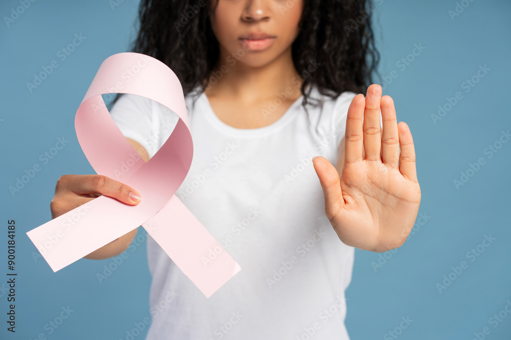 Woman showing pink ribbon and making stop gesture against blue background closeup selective focus Woman showing pink ribbon and making stop gesture against blue background closeup selective focus