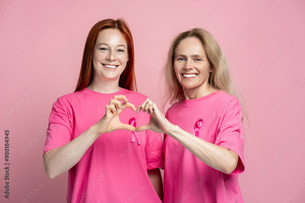 Two smiling women wearing pink t shirts with pink ribbons making heart shape with their hands Two smiling women wearing pink t shirts with pink ribbons making heart shape with their hands