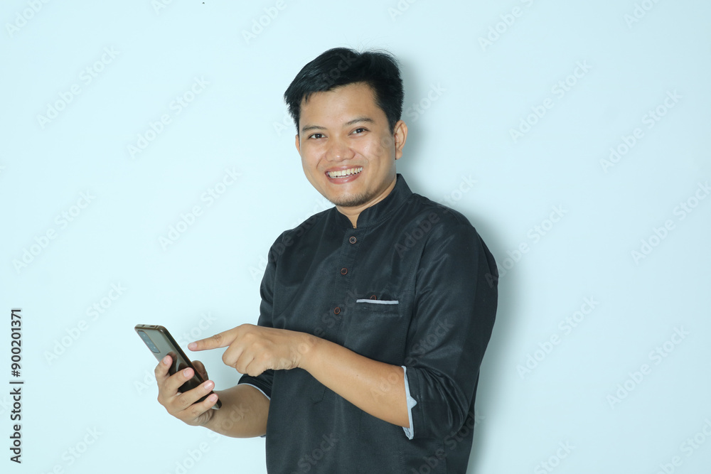 Moslem Asian man showing smiling happy while touching his mobile phone screen and looking at the camera. Wearing a black shirt Moslem Asian man showing smiling happy while touching his mobile phone screen and looking at the camera. Wearing a black shirt