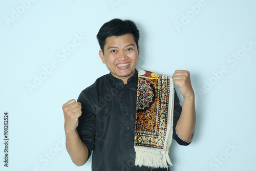 Moslem Asian man showing excited expression with both fist clenched. Wearing a black shirt