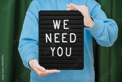 We need you. Neon sign. Brick wall at night with the text "We need you" in blue neon letters: announcement message, hiring, recruitment.