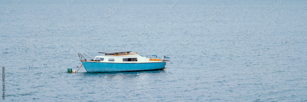 A lonely old blue boat with orange elements moored on a lake far from the shore.