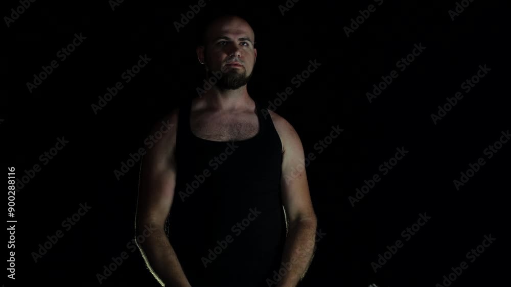 A man lifts a barbell in the dark. Newbie starts bodybuilding in a black t-shirt. Working out at night, he flexes his biceps. Bald man doing sports A man lifts a barbell in the dark. Newbie starts bodybuilding in a black t-shirt. Working out at night, he flexes his biceps. Bald man doing sports