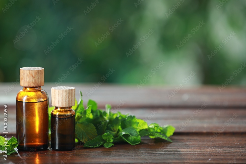 Bottles of mint essential oil and fresh leaves on wooden table, space for text Bottles of mint essential oil and fresh leaves on wooden table, space for text