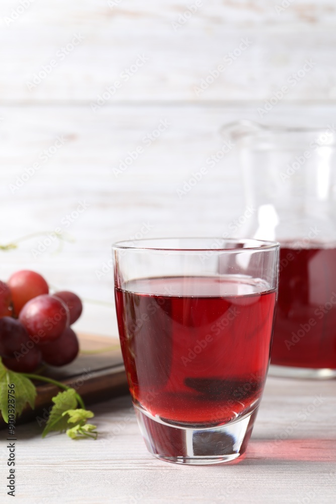 Tasty grape juice in glass, leaves and berries on light wooden table Tasty grape juice in glass, leaves and berries on light wooden table