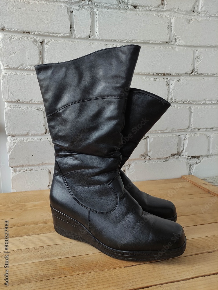 Black leather women's winter boots on a wooden background Black leather women's winter boots on a wooden background
