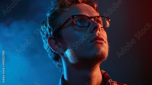 A nerdy guy with glasses smiles against a dark blue background, showcasing his unique personality and style with a friendly expression. photo