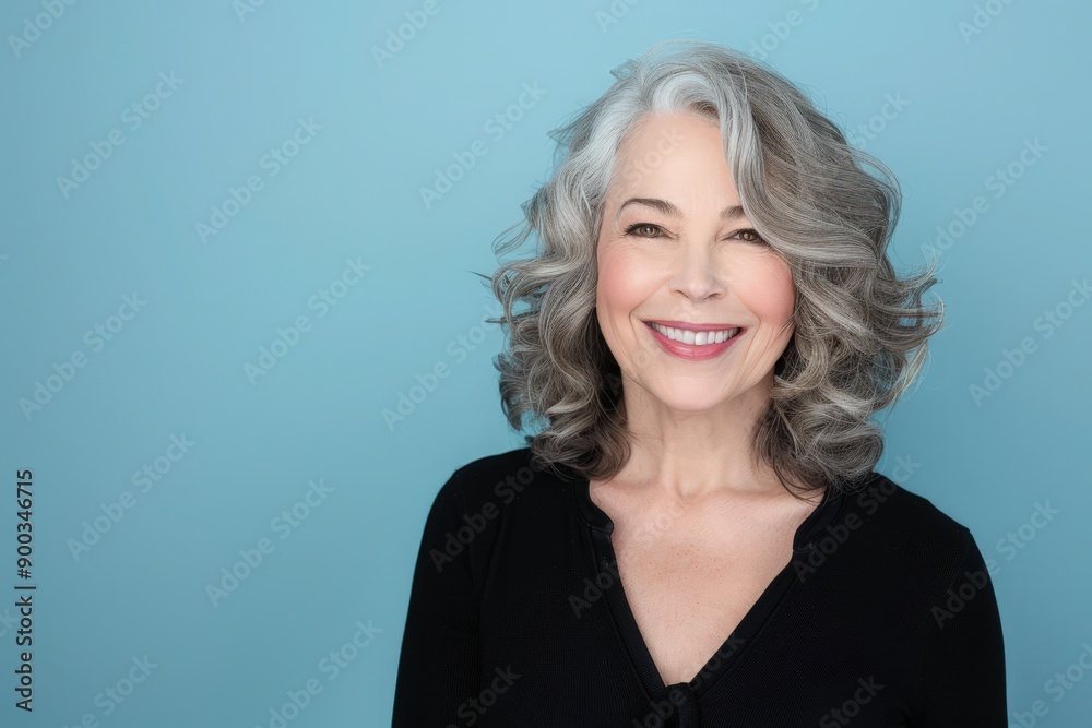 A cheerful woman with curly grey hair radiates warmth and positivity, her bright smile contrasting beautifully against a serene blue backdrop. A cheerful woman with curly grey hair radiates warmth and positivity, her bright smile contrasting beautifully against a serene blue backdrop.