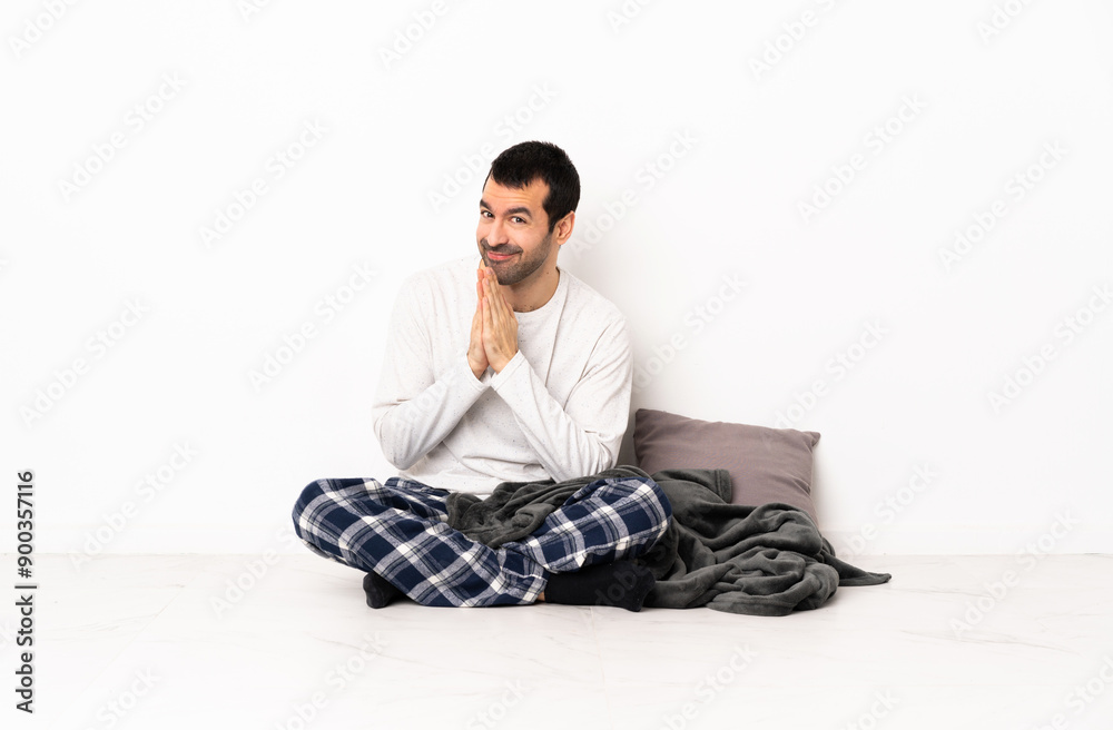 Caucasian man in pajamas sitting on the floor at indoors keeps palm together. Person asks for something Caucasian man in pajamas sitting on the floor at indoors keeps palm together. Person asks for something