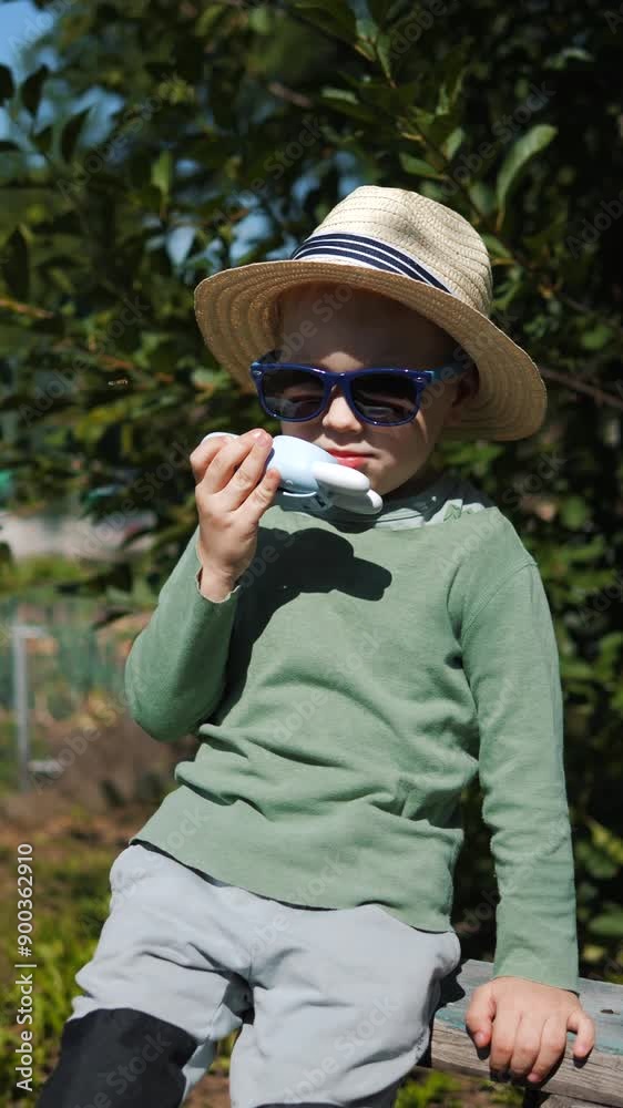Little boy in a straw hat and sunglasses walking and playing in the garden Little boy in a straw hat and sunglasses walking and playing in the garden