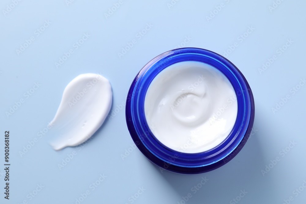 Face cream in jar and smear on light blue background, top view Face cream in jar and smear on light blue background, top view