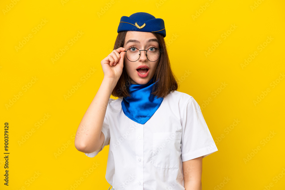 Airplane stewardess Ukrainian woman isolated on yellow background with glasses and surprised Airplane stewardess Ukrainian woman isolated on yellow background with glasses and surprised