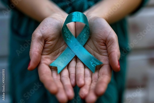 Close-up of beautiful human hands holding a teal ribbon to support cervical cancer awareness. photo