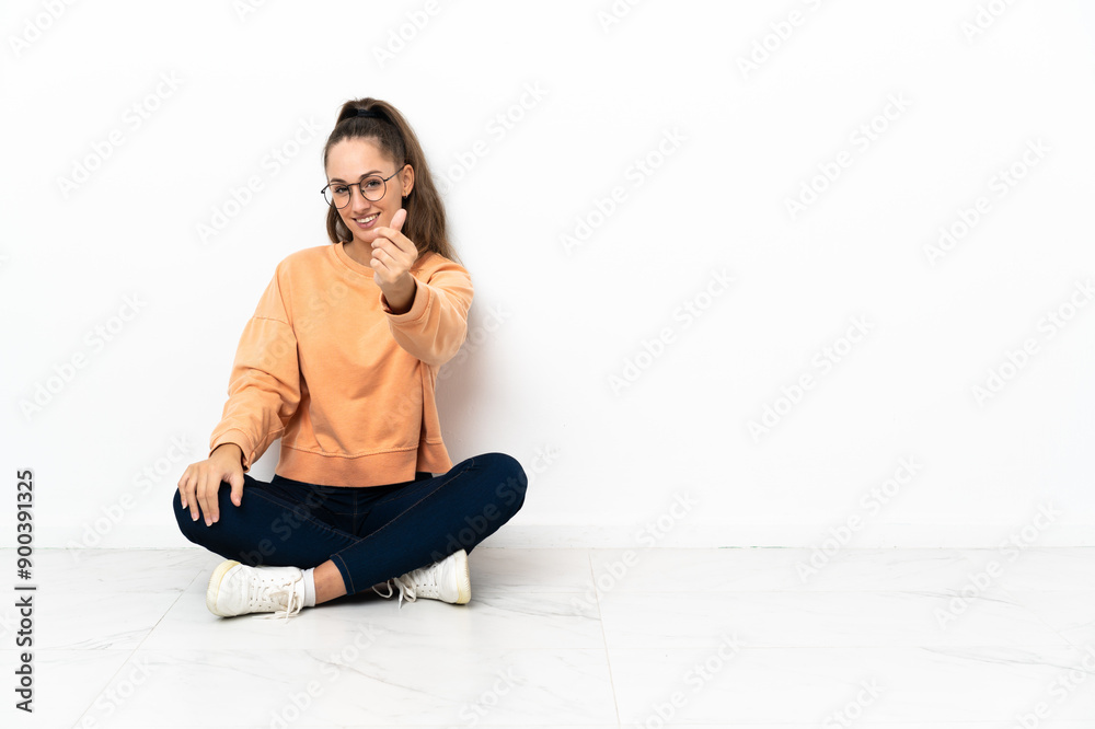 Young woman sitting on the floor making money gesture Young woman sitting on the floor making money gesture