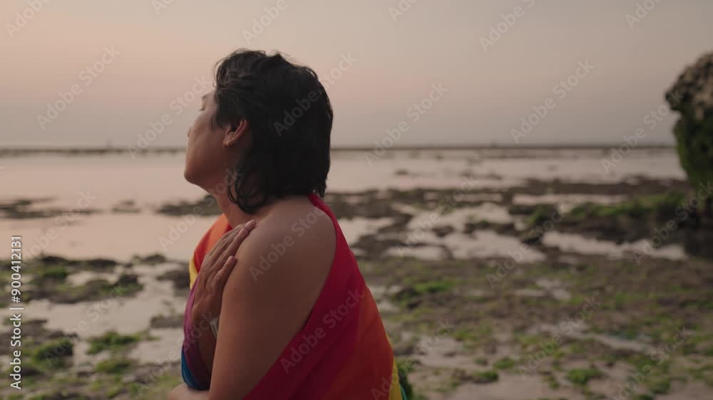 Silhouette Dark Skinned Southeast Asian LGBT Gay Man Sitting on the Beach Rock with Rainbow Pride Flag during Sunset Silhouette Dark Skinned Southeast Asian LGBT Gay Man Sitting on the Beach Rock with Rainbow Pride Flag during Sunset