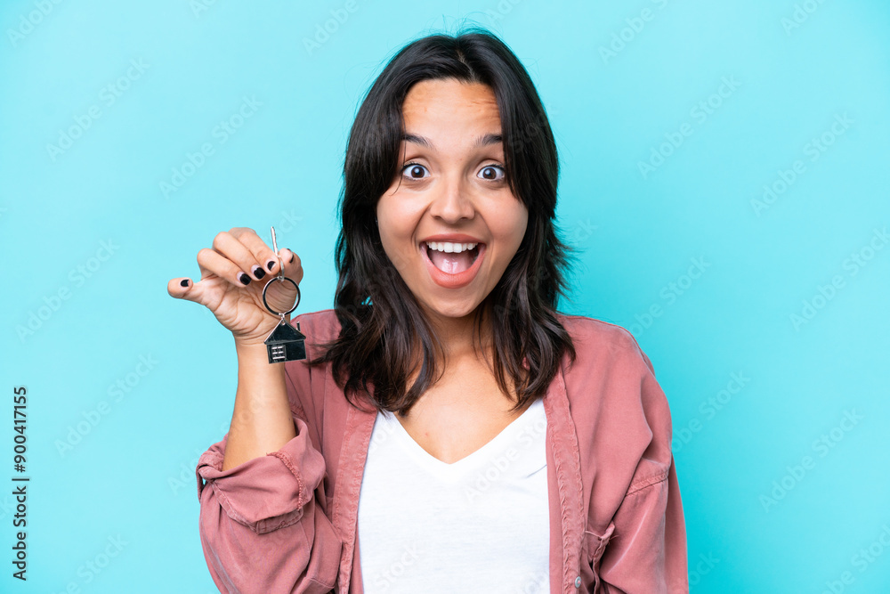 Young hispanic woman holding home keys isolated on blue background with surprise facial expression Young hispanic woman holding home keys isolated on blue background with surprise facial expression