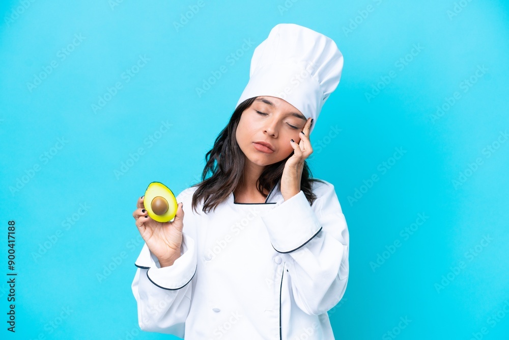 Young hispanic chef woman holding avocado isolated on blue background with headache Young hispanic chef woman holding avocado isolated on blue background with headache