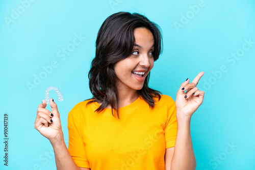 Young hispanic woman holding invisible braces isolated on blue background intending to realizes the solution while lifting a finger up