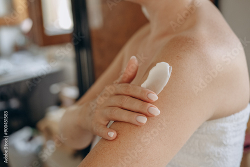 close up female hands and a smear of cream  or lotion or serum  on the skin, woman applies moisturizing cream or lotion after showering, daily body skin care routine  photo