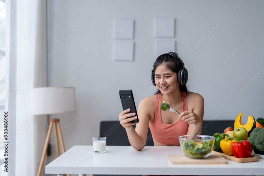 Smiling asian fitness woman eating salad and having video call on smartphone at home Smiling asian fitness woman eating salad and having video call on smartphone at home