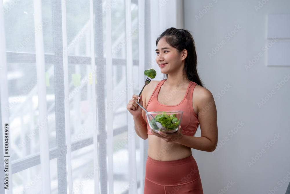 Young asian woman eating salad and looking through the window at home Young asian woman eating salad and looking through the window at home